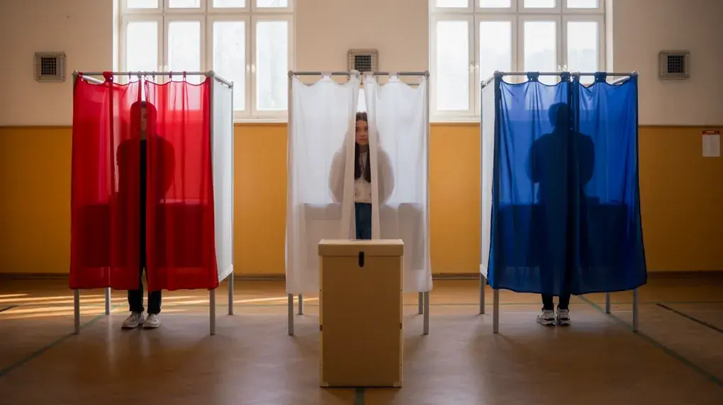 Symbolbild: Drei Wahlkabinen mit farbigen Vorhängen bei einer Probewahl in der Turnhalle