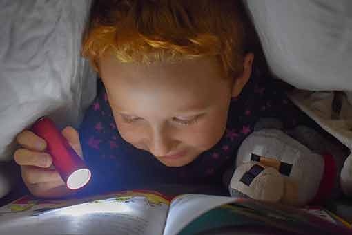 Kind liest unter Bettdecke